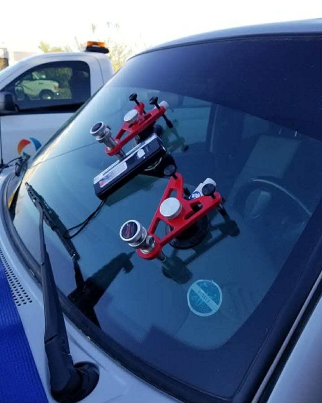 Red rock chip repair injection tool clamped onto a windshield, mid-repair.