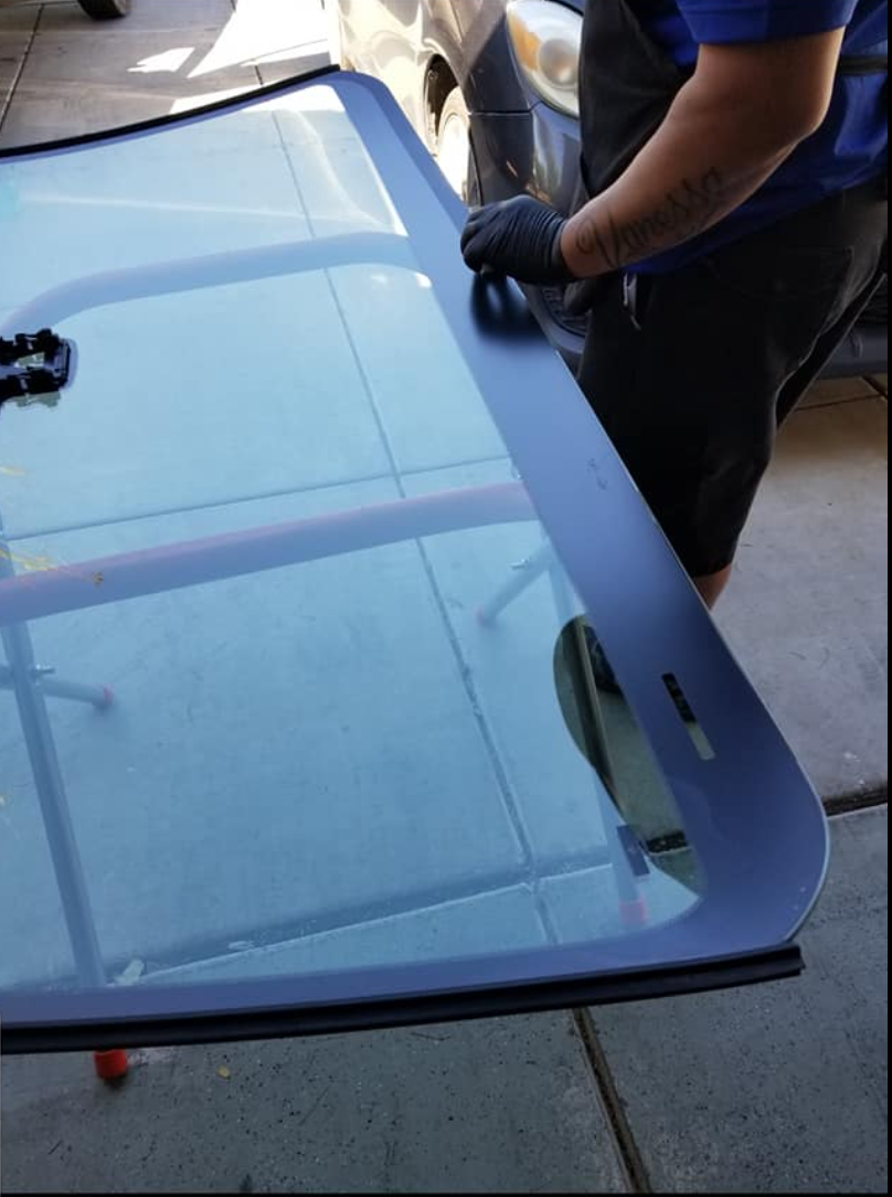 Close-up of gloved hands handling a fresh windshield panel.